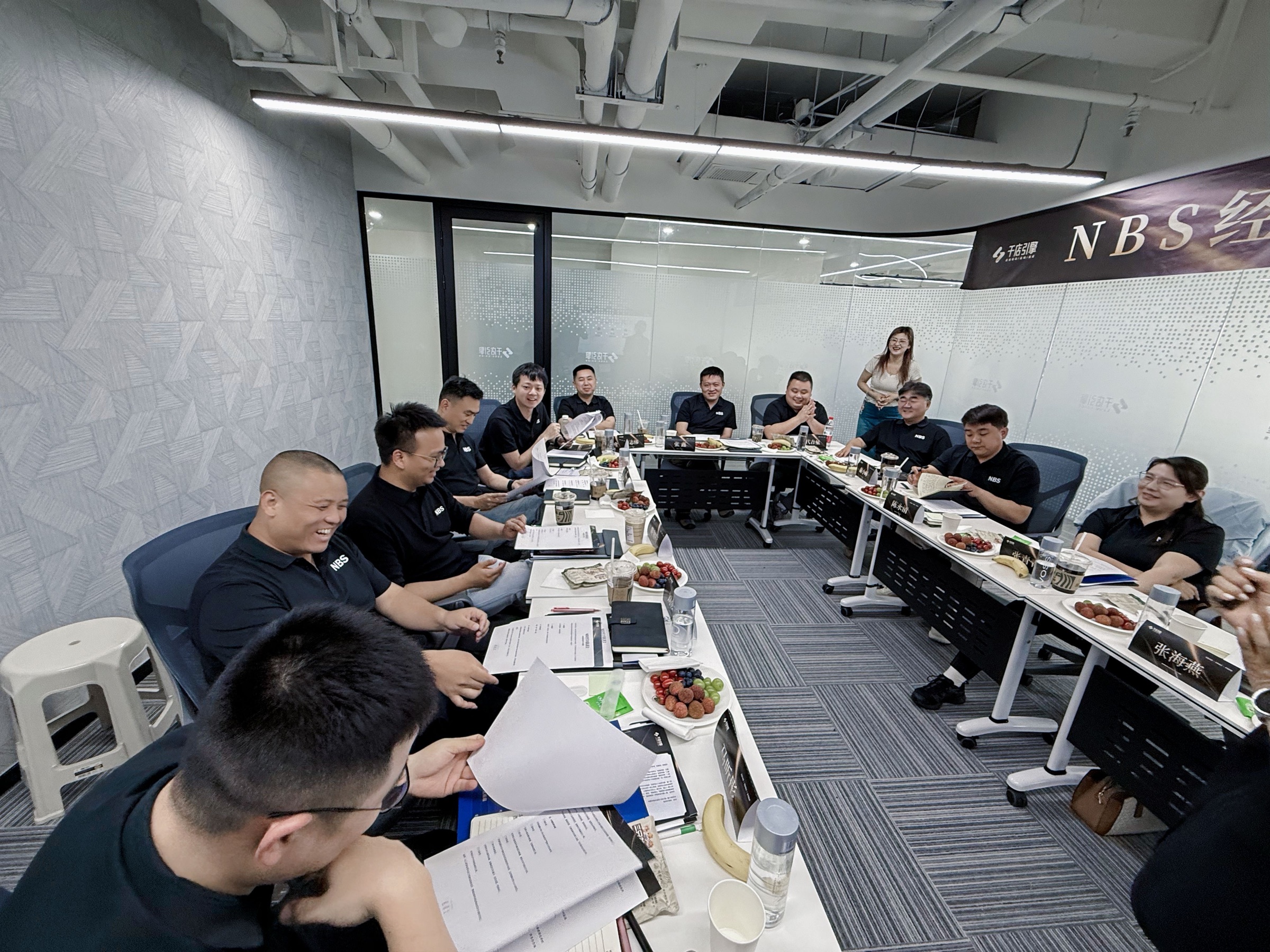 NBS经营者会议现场，成员围桌阅读材料并交流